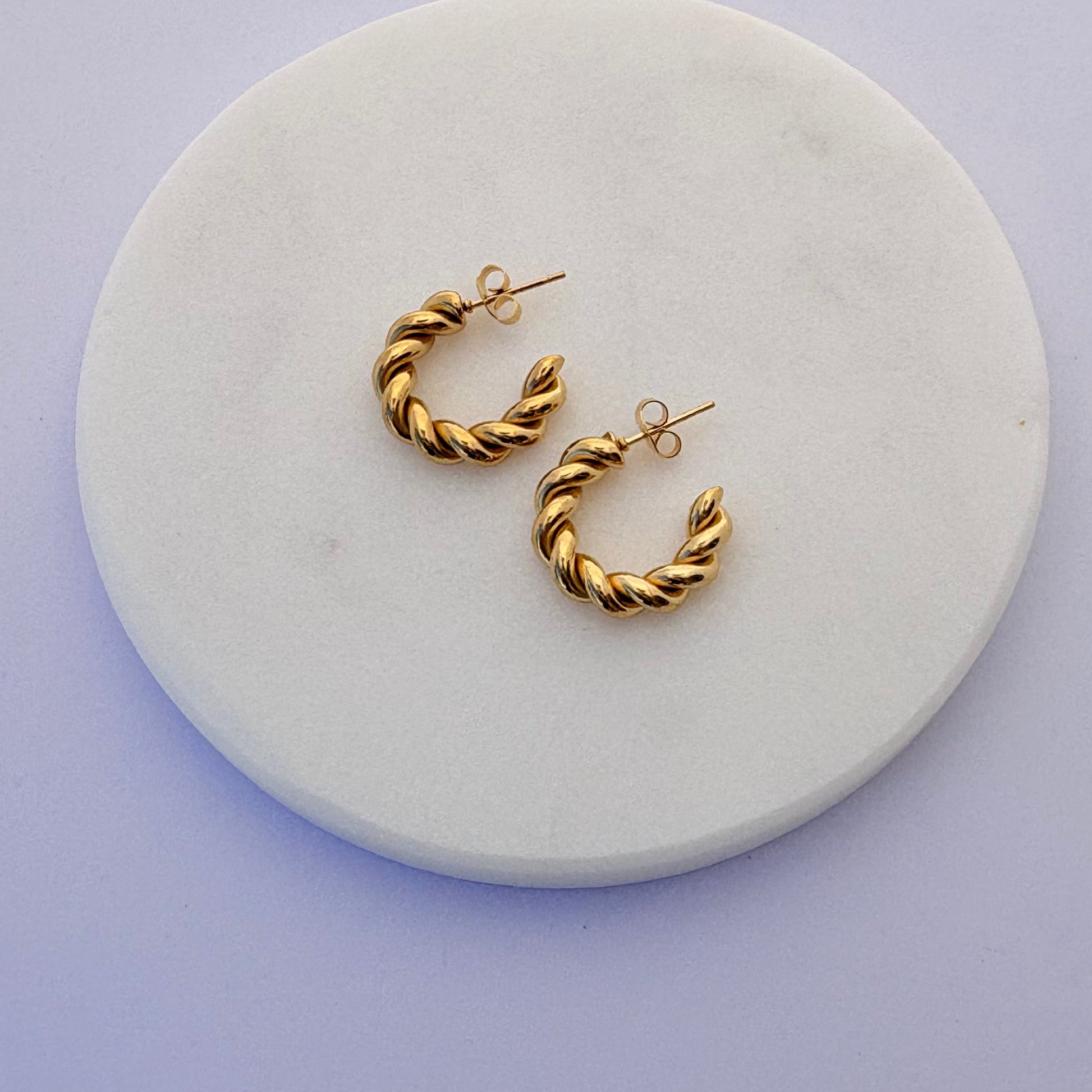 Gold hoop earrings on a round white marble stand with a light purple background