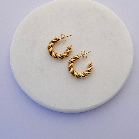 Gold hoop earrings on a round white marble stand with a light purple background