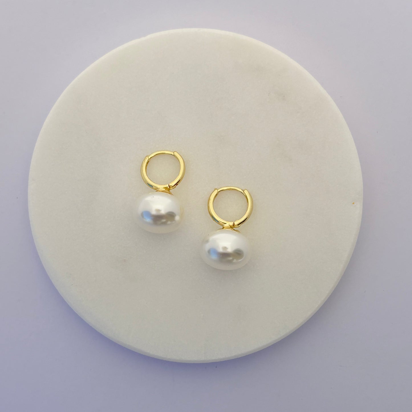 Pair of gold hoop earrings with pearls on a round white stone surface.