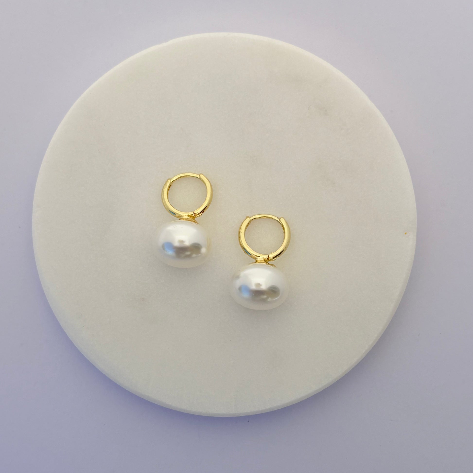 Pair of gold hoop earrings with pearls on a round white stone surface.
