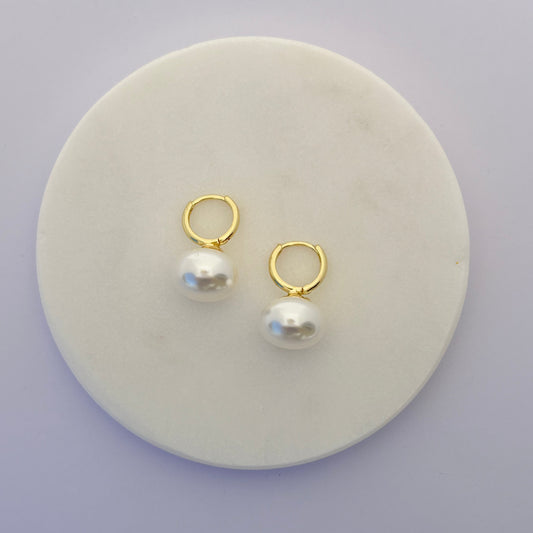 Pair of gold hoop earrings with pearls on a round white stone surface.