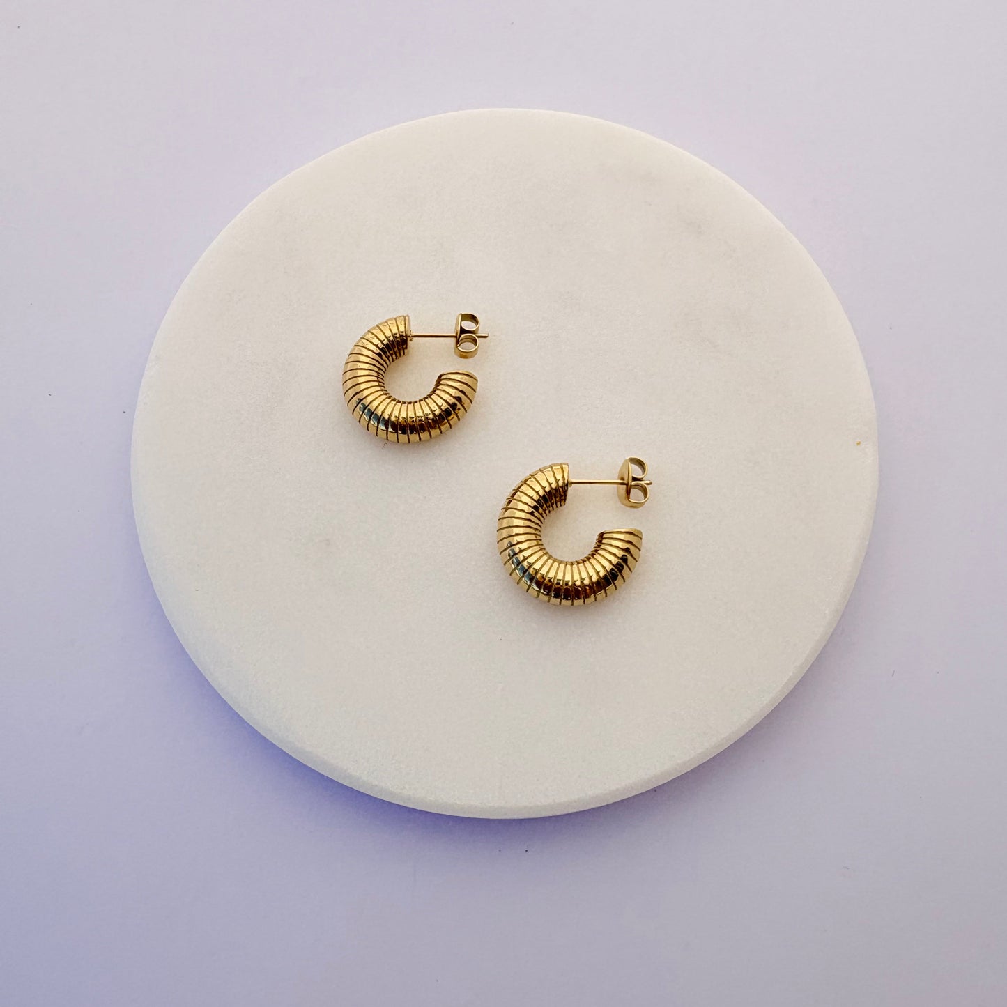 Gold hoop earrings on a round white stone surface with a light purple background