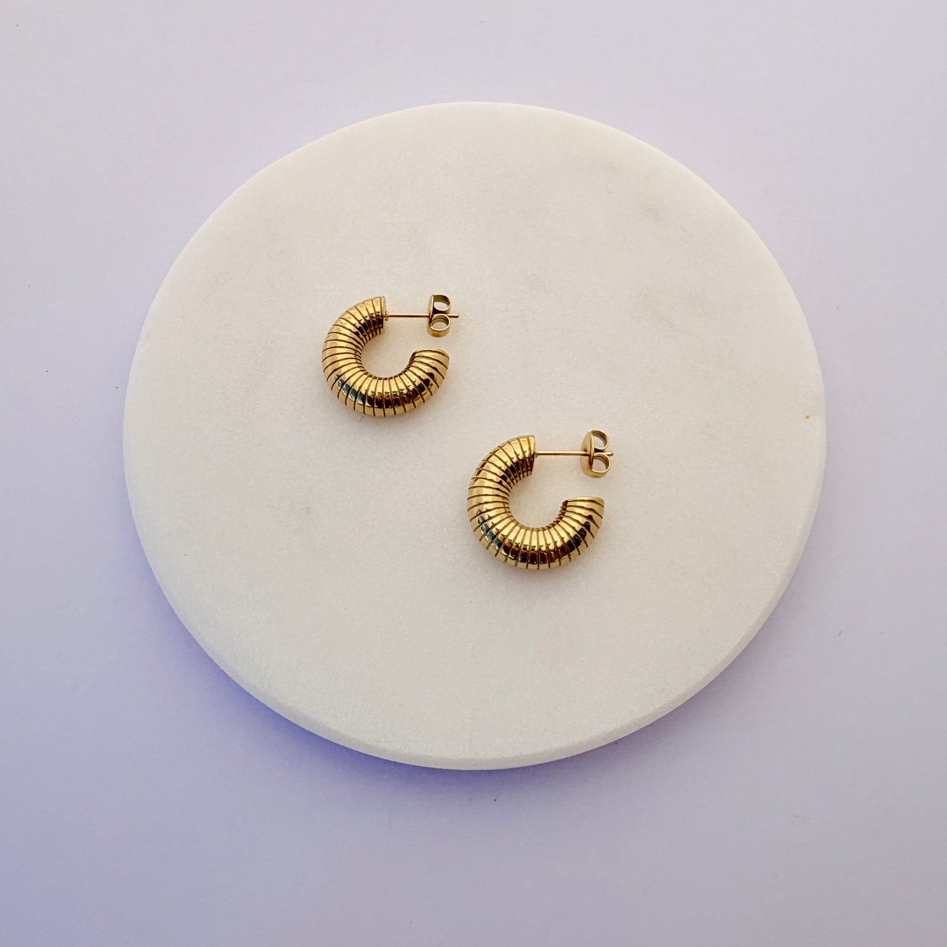Gold hoop earrings on a round white stone surface with a light purple background