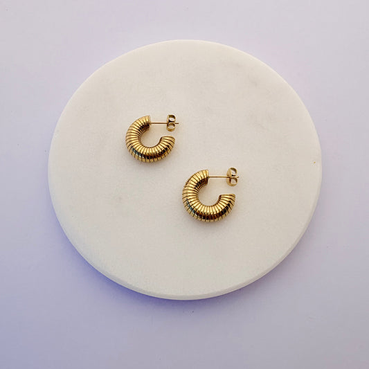 Gold hoop earrings on a round white stone surface with a light purple background