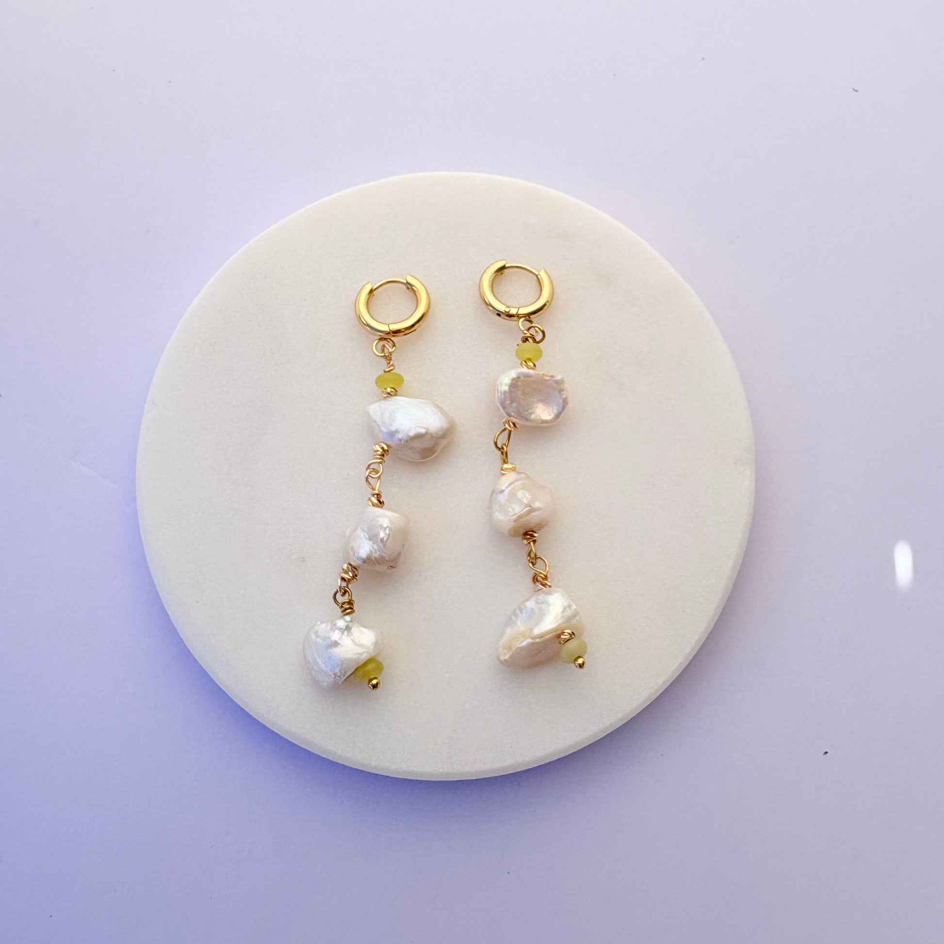Two pearl and gold bracelet sets on a round white stone surface with a light purple background.