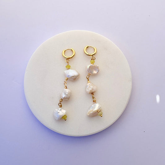 Two pearl and gold bracelet sets on a round white stone surface with a light purple background.
