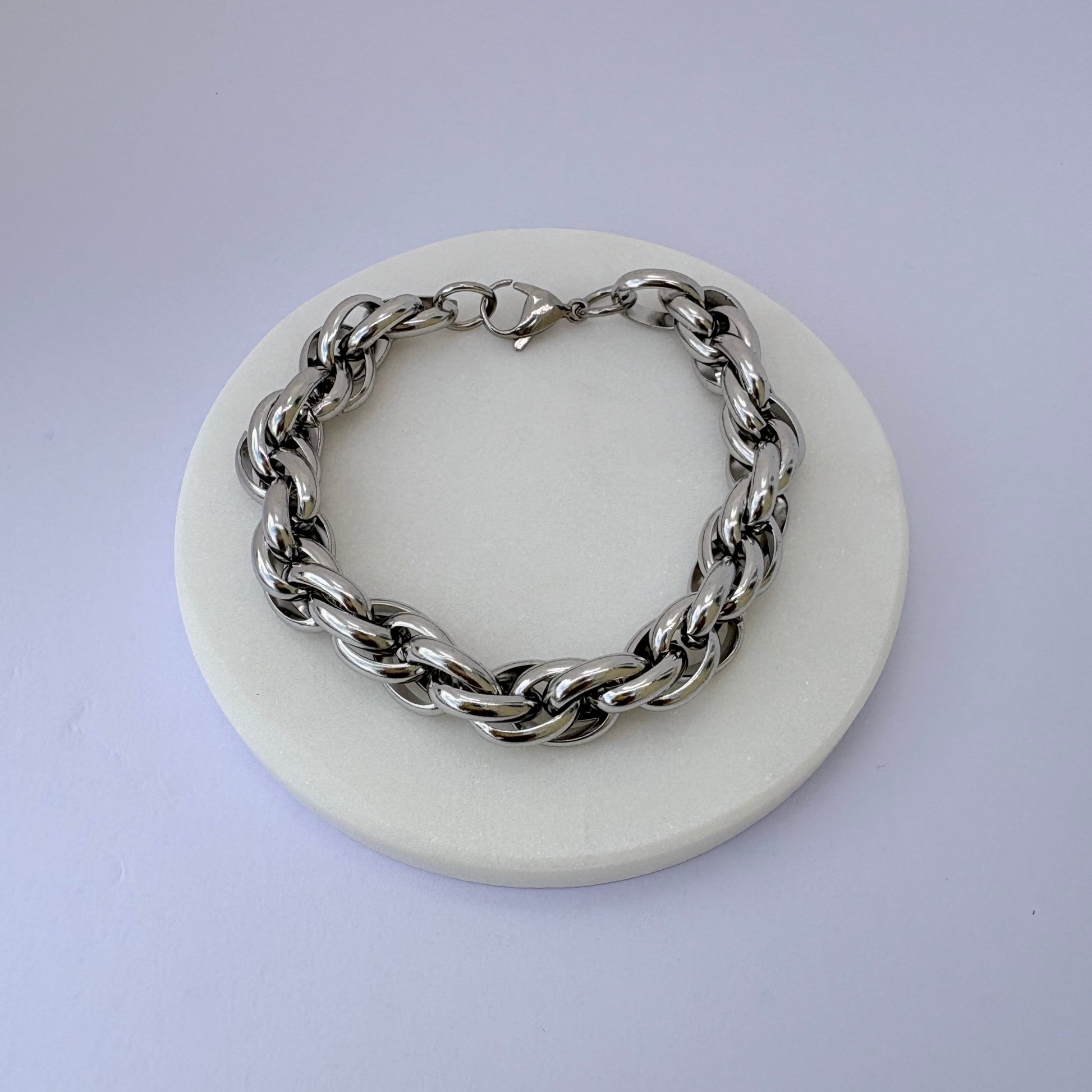 Silver chain bracelet on a white circular stand with a light purple background