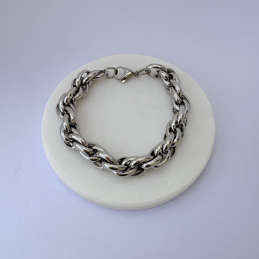 Silver chain bracelet on a white circular stand with a light purple background