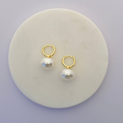 Pair of gold hoop earrings with pearls on a round white stone surface.